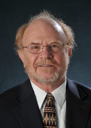 Headshot of am an smiling wearing wire-rim glasses and a dark suitcoat and tie with a white shirt.