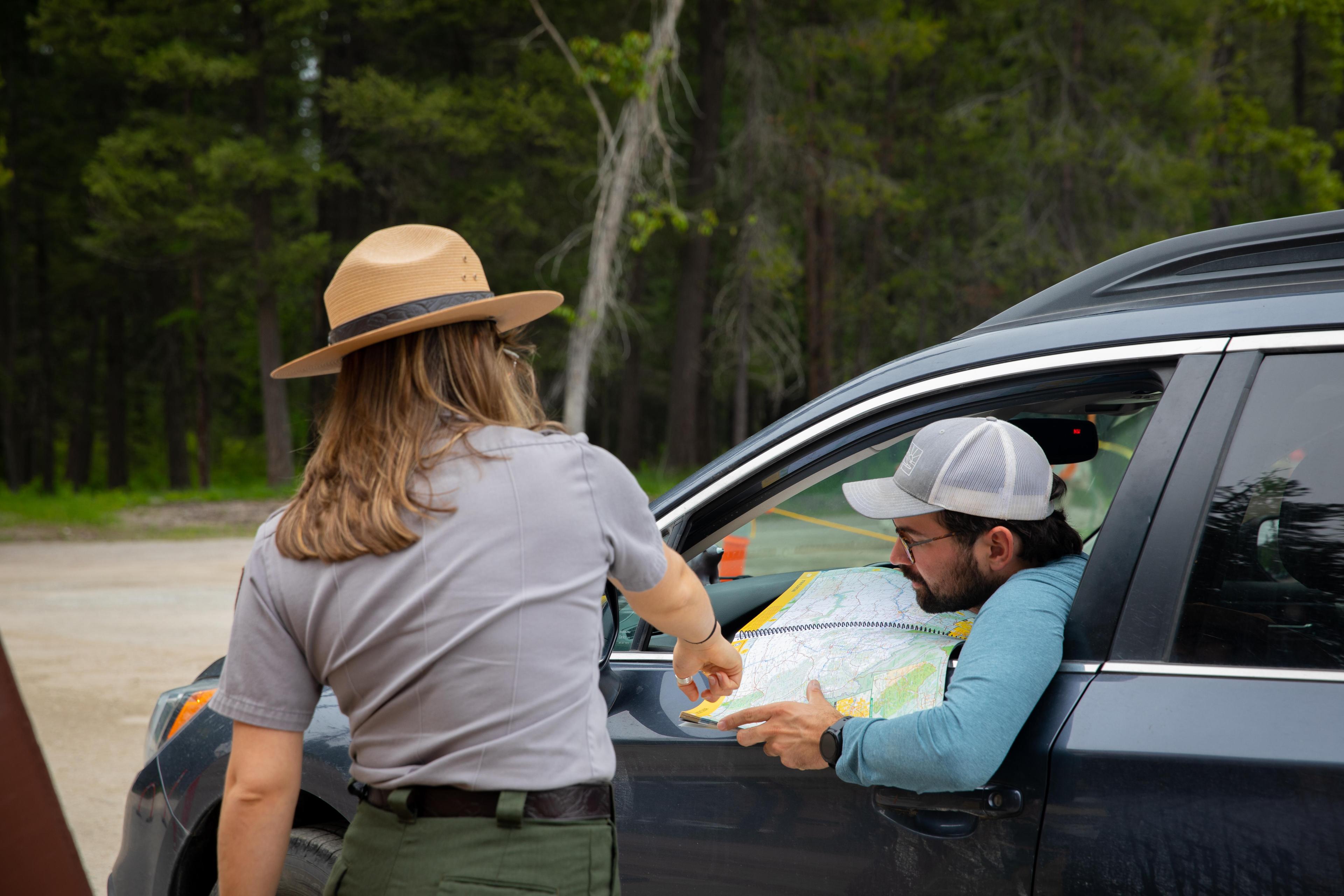 A ranger points to a map that a man in a car is holding.